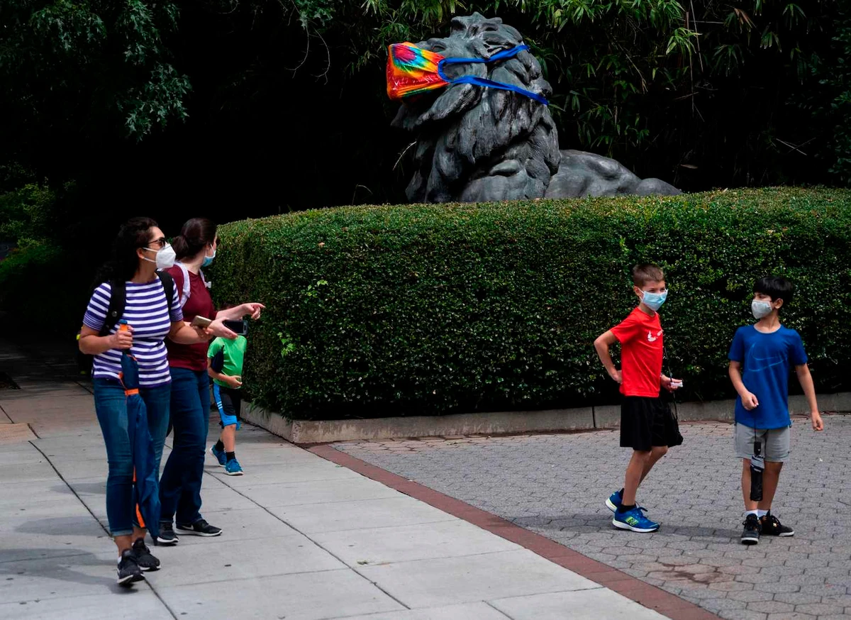 A family walks past one of the lion statues at the entrance on the opening day of the Smithsonian National Zoo in Washington, DC on July 24, 2020, after it closed due to COVID-19 outbreak in March. (AFP)