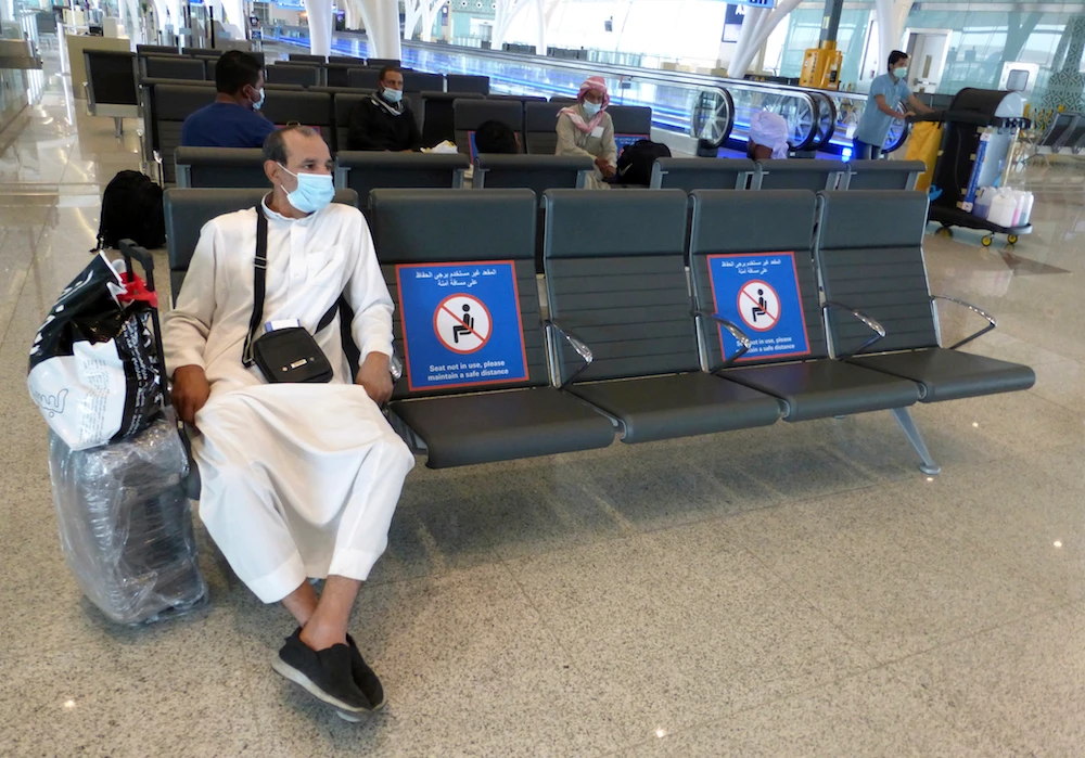 A passenger sits beside posters displaying social distancing restrictions as he waits for his flight at the King Abdulaziz International Airport in Jeddah, Saudi Arabia on Tuesday July 28, 2020. (AP)