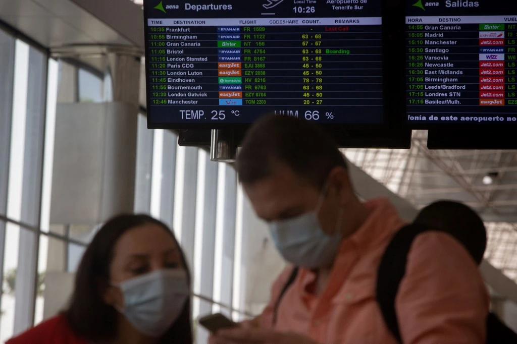 British tourists walk past arrival and departure screens upon their arrival to the Tenerife Sur Reina Sofia airport on the Canary Island of Tenerife on July 28, 2020. (AFP)