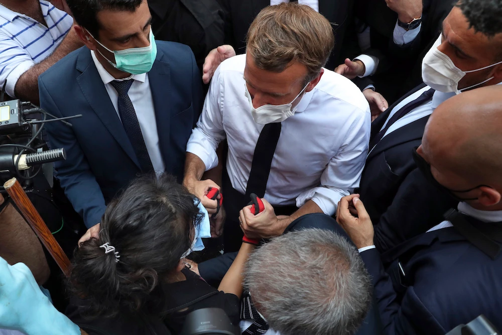 French President Emmanuel Macron, holds hand with a woman as he visits the Gemayzeh neighborhood, which suffered extensive damage from an explosion on Tuesday that hit the seaport of Beirut, Lebanon, Thursday, Aug. 6, 2020. (AP)