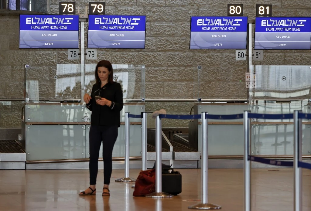A passenger using her phone next to screens displaying the flight number of the first-ever commercial flight from Israel to the UAE at the Ben Gurion Airport. (AFP)