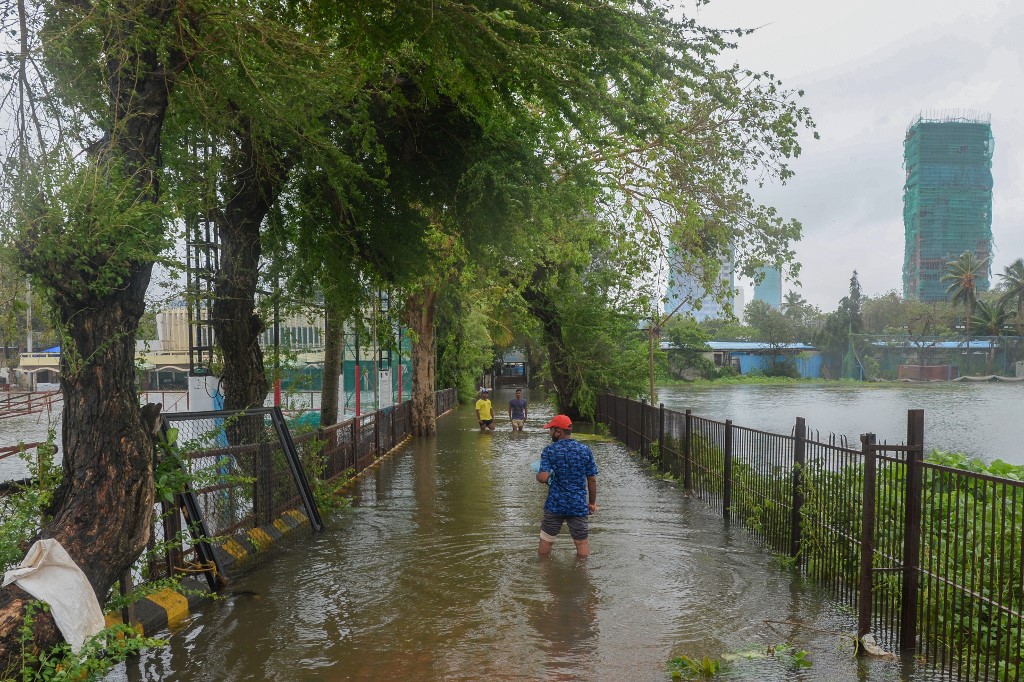 People wade through a waterlogged pathway next to flooded cricket grounds following recent heavy monsoon rains in Mumbai on August 6, 2020. (AFP)