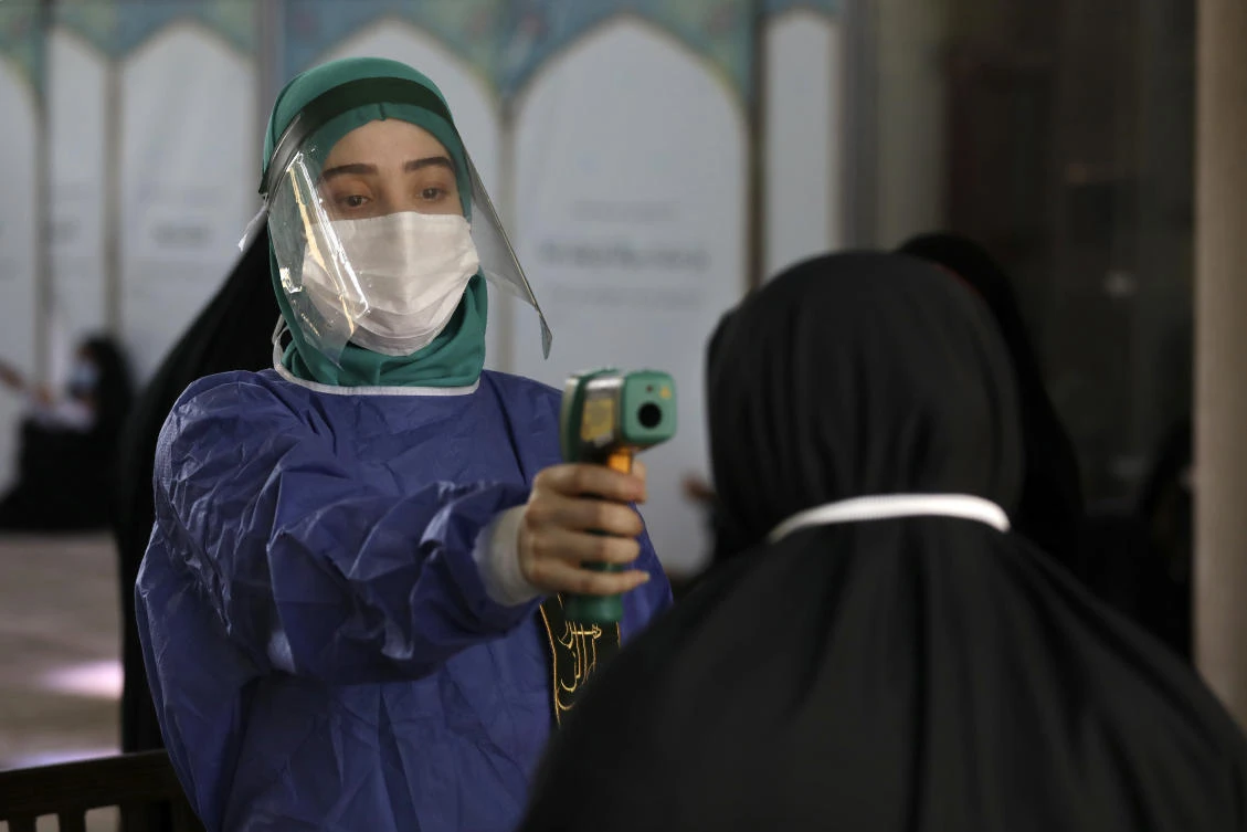 A volunteer wearing protective gear to help prevent the spread of the coronavirus checks temperature of a worshipper as she enters mosque of Tehran University to pray during Arafat Day, Iran, Thursday, July 30, 2020. (AP)