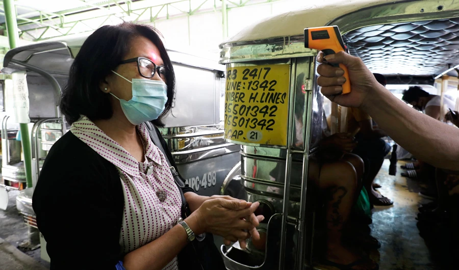 Temperature is taken before riding a passenger jeepney to help curb the spread of COVID-19 as drivers at Quezon city terminal were allowed back on the road. (AP)