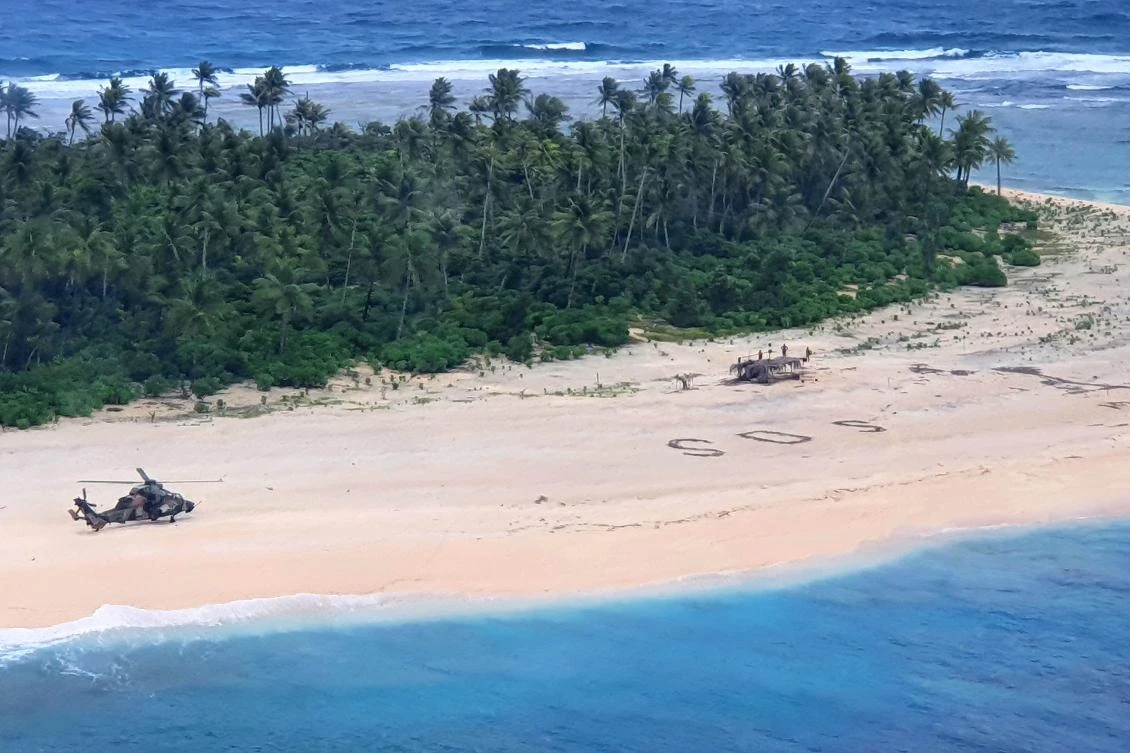 This handout photo taken on August 2, 2020 shows an Australian Army ARH Tiger helicopter landing near the letters "SOS" (C) on a beach on Pikelot Island where three men were found in good condition after being missing for three days. Three Micronesian sailors stranded on a tiny island in the remote Western Pacific were rescued after Australian and US warplanes spotted a giant "SOS" they had scrawled on the beach, officials said. (AFP)