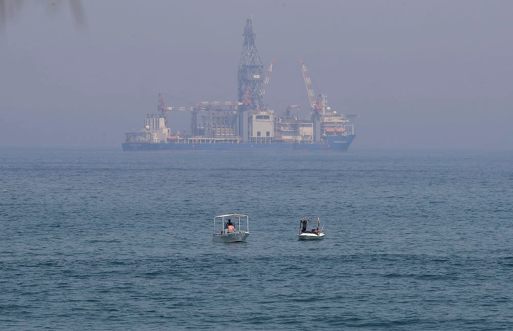 Lebanese people sit in boats in the Mediterranean sea as the Tungsten Explorer, a drillship to explore for oil and gas off the coast of Lebanon, is seen in the background in Dbayeh north of the capital Beirut. (File/AFP)