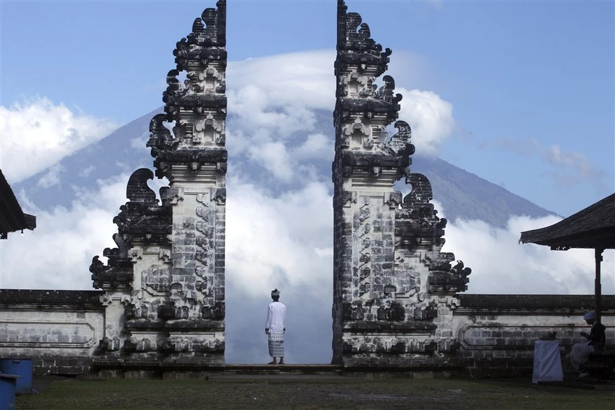 A Balinese man stands at the gate of Lempuyang temple looking towards Mount Agung volcano, in Karangasem Regency, Bali, Indonesia. (AP Photo)