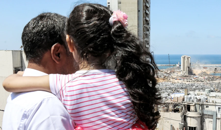 Makhoul Mohammad al-Hamad, 43, stands holding his six-year-old daughter Sama from their apartment as they watch diggers removing earth at the blast site next to the silos at the port of Beirut on August 16, 2020, in the aftermath of the massive explosion there that ravaged Lebanon's capital. (AFP)