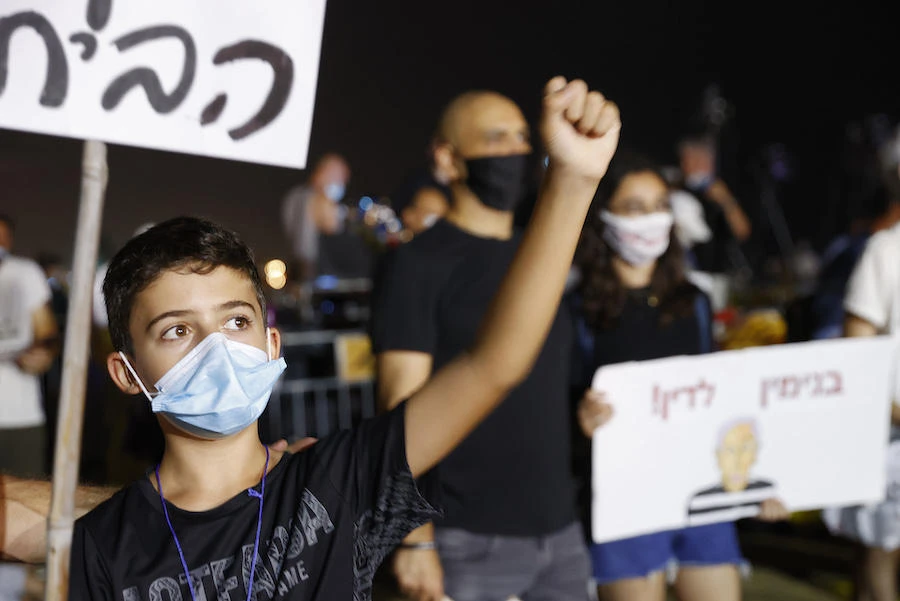 A boy, mask-clad due to the COVID-19 coronavirus pandemic, raises his fist while chanting slogans during a demonstration against the Israeli government in the Mediterranean coastal city of Tel Aviv on August 1, 2020. (AFP)