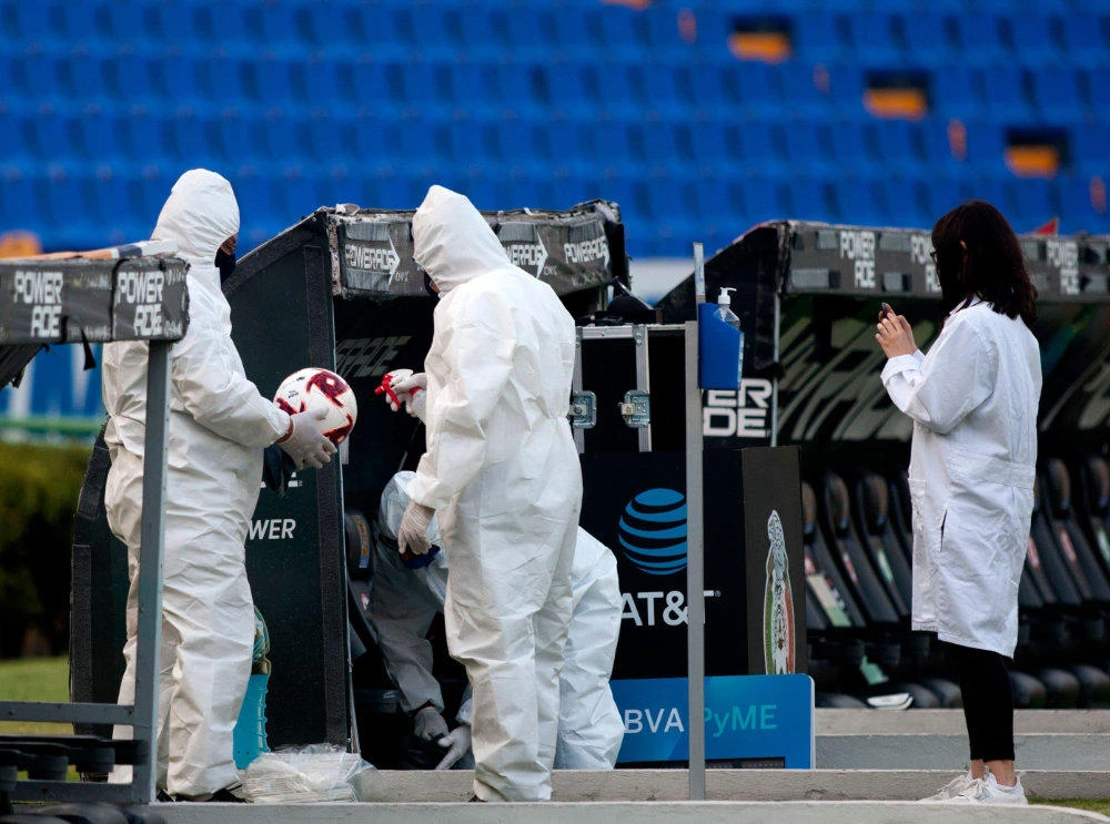 Employees wearing disinfect a football at the empty Universitario stadium during the halftime of the Mexican Apertura 2020 football tournament match between Tigres and Pumas in Monterrey, Mexico, on August 22, 2020, amid the COVID-19 coronavirus pandemic. (AFP / Julio Cesar Aguilar)