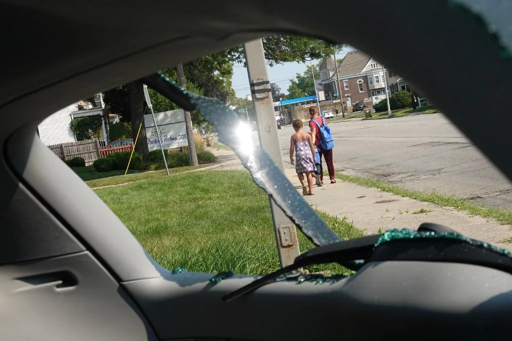 People walk past a vandalized vehicle at a used car lot where a person was reported to have been shot by Kyle Rittenhouse during a third night of unrest in Kenosha, Wisconsin. (Getty Images/AFP)