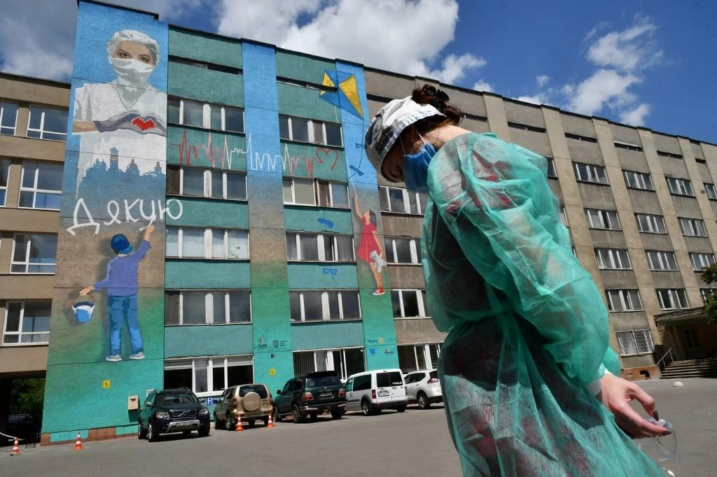 A woman wearing personal protective equipment (PPE) stands in front of a graffiti painted on Lviv emergency hospital wall. (File/AFP)