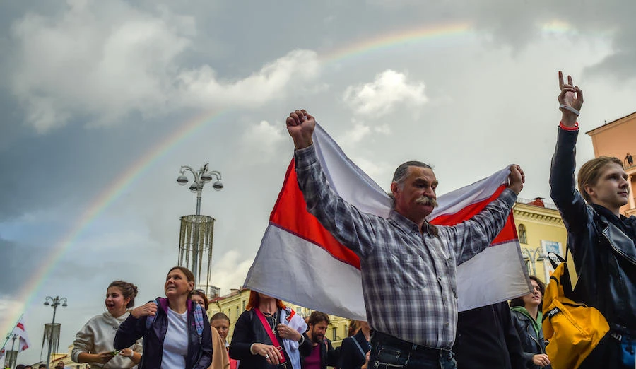 A man holds a historical white-red-white flag of Belarus with a rainbow in the back as opposition supporters rally to protest against disputed presidential elections results in Minsk on August 27, 2020. (File/AFP)