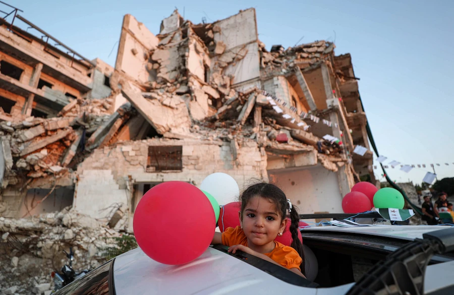 A girl looks on as she stands through the skylight of a vehicle while Syrians demonstrate nearby amidst buildings destroyed in previous bombardment in the town of Ariha in the rebel-held northwestern Idlib province on August 28, 2020. (AFP)