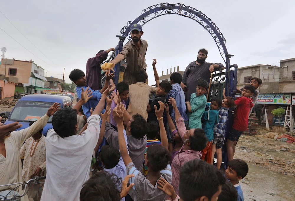 People jostle to get free food at an inundated residential area caused by heavy monsoon rains, in Karachi, Pakistan, Friday, Aug. 28, 2020. (AP)