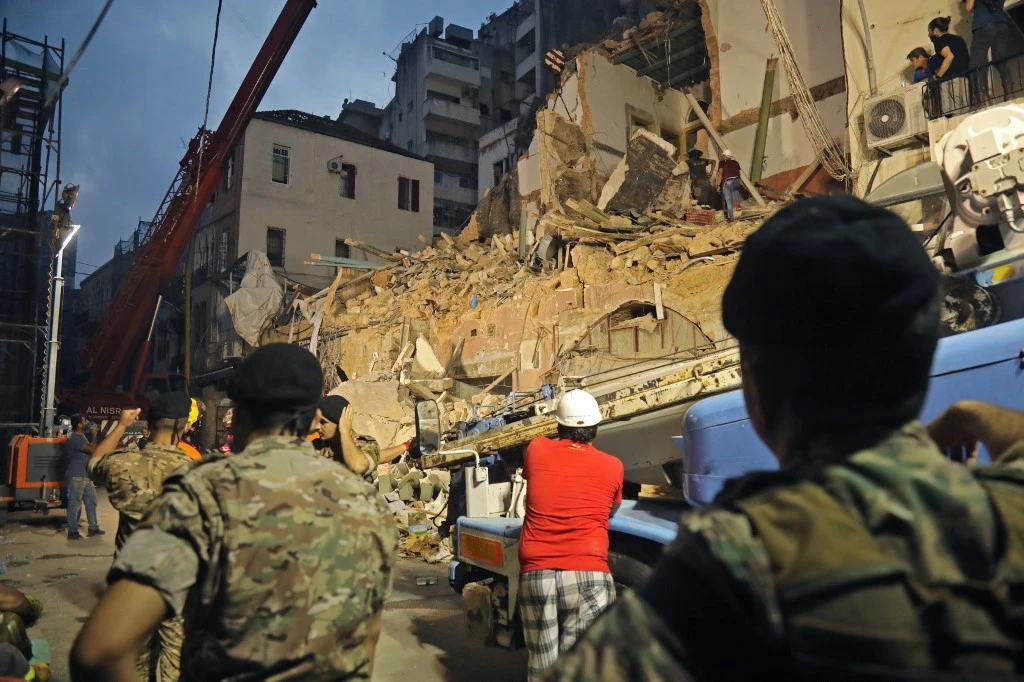 Lebanese and Chilean rescuer workers watch as a crane lifts pieces of cement from a badly damaged building in Beirut in search of possible survivors early on September 4, 2020. (AFP)
