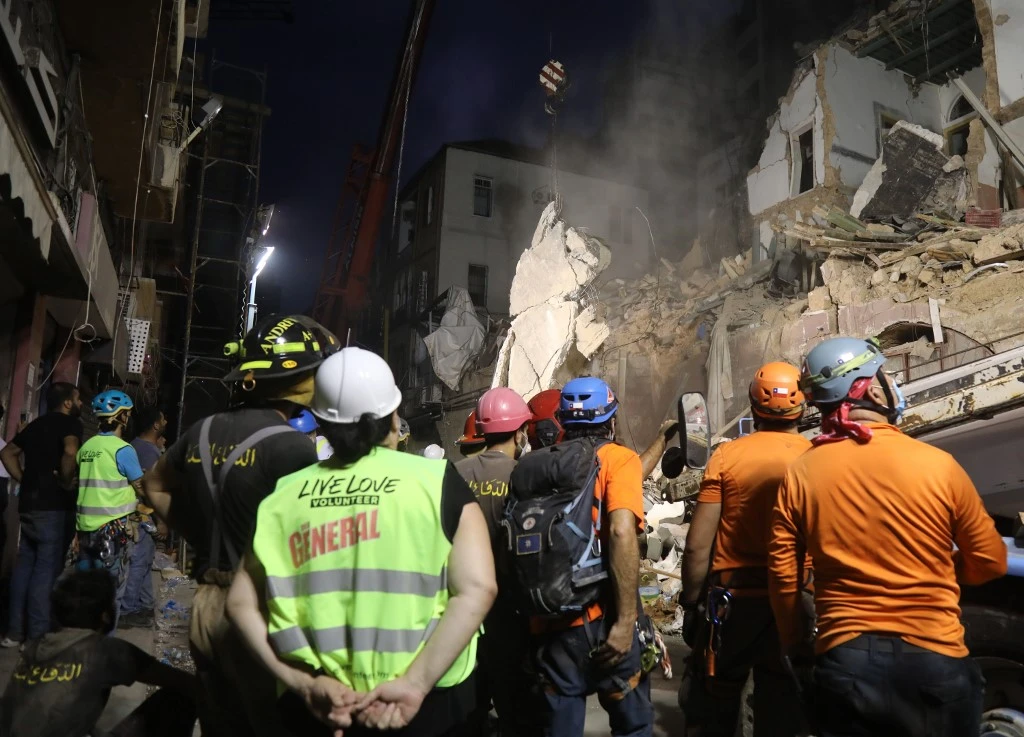 Lebanese and Chilean rescuer workers watch as a crane lifts pieces of cement from a badly damaged building in Beirut in search of possible survivors early on September 4, 2020. (AFP)