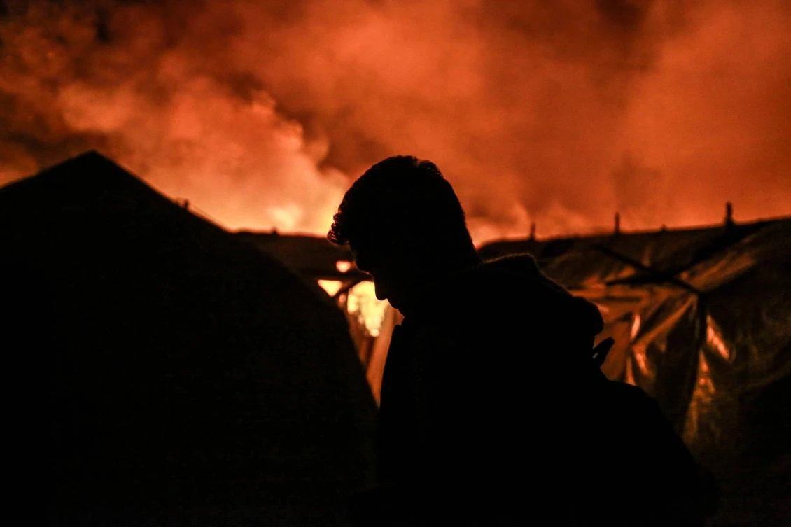 A migrant stands near tents as a fire burns in the Moria camp on the island of Lesbos on September 9, 2020. The migrant camp of Moria, on the Greek island of Lesbos, has been partially evacuated after a fire that broke out early on September 9, Greek firefighters announced. (AFP)