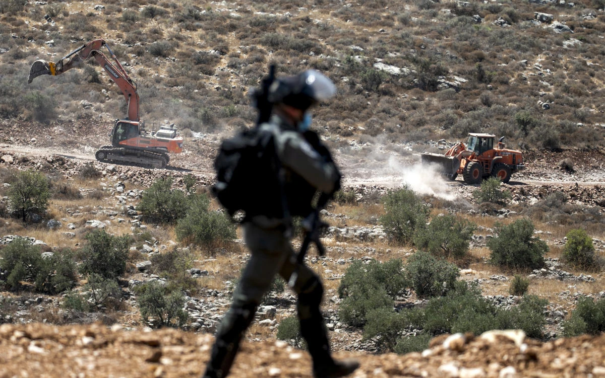 An Israeli soldier walks while in the background Israeli earth movers and bulldozers are seen near the village of Shoufah, southeast of Tulkarm in the occupied West Bank on August 20, 2020, as Palestinians protest against the clearing of lands to expand Israeli settlements. (File/AFP)