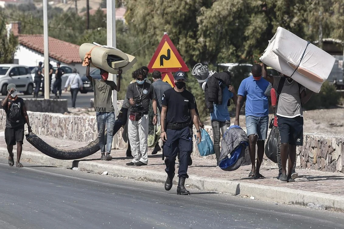 A policeman escorts migrants carrying their belongings who remained near the burnt Moria camp toward a new temporary camp, set up to shelter refugees a few days after a fire destroyed the camp, on the island of Lesbos on September 13, 2020. (AFP)