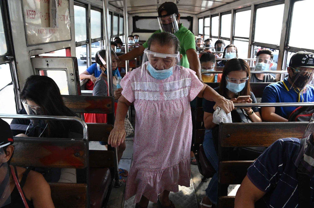In this photo taken on Sept. 8, 2020, an elderly woman wearing a face shield boards a bus in Manila. (AFP / Ted Aljibe)