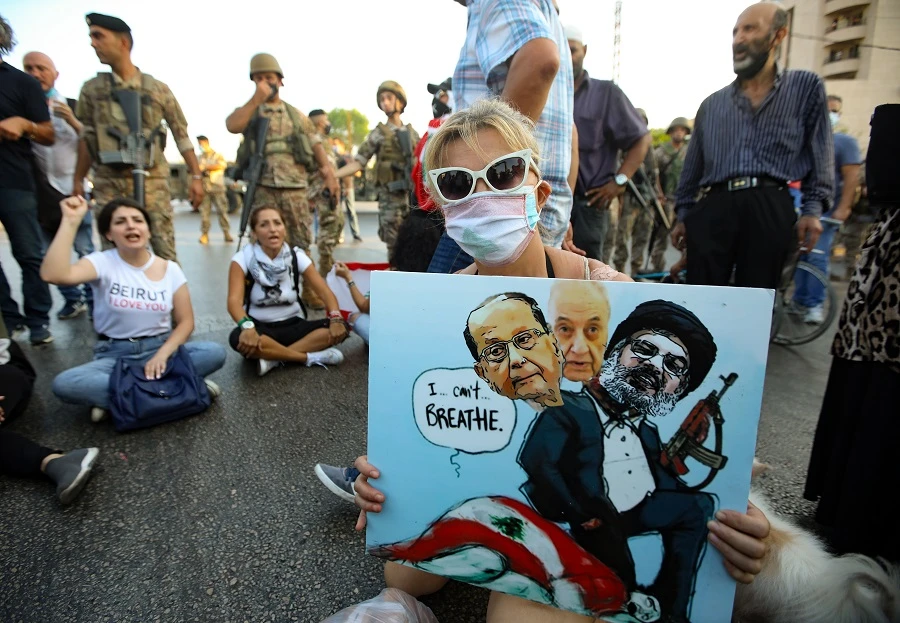 A Lebanese anti government protester holds a placard with a cartoon of (L-R) President Michel Aoun, Parliament Speaker Nabih Berri and head of the Shiite movement Hezbollah Hassan Nasrallah. (Photo by ANWAR AMRO / AFP)
