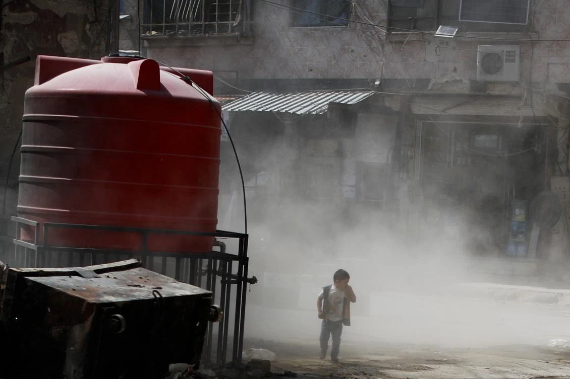 A Syrian boy walks amid a cloud of dust as a bulldozer removes debris from destroyed buildings, in the town of Douma, eastern Ghouta region, near the Syrian capital Damascus, July 15, 2018. (AP Photo)