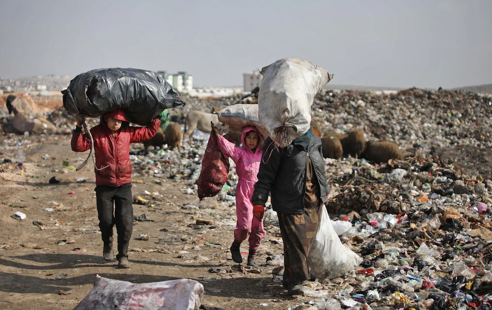 A displaced Syrian woman and children carry over their heads bags of collected trash at a landfill outside a camp in Kafr Lusin near the border with Turkey in Idlib province in northwestern Syria. (AFP/File Photo)