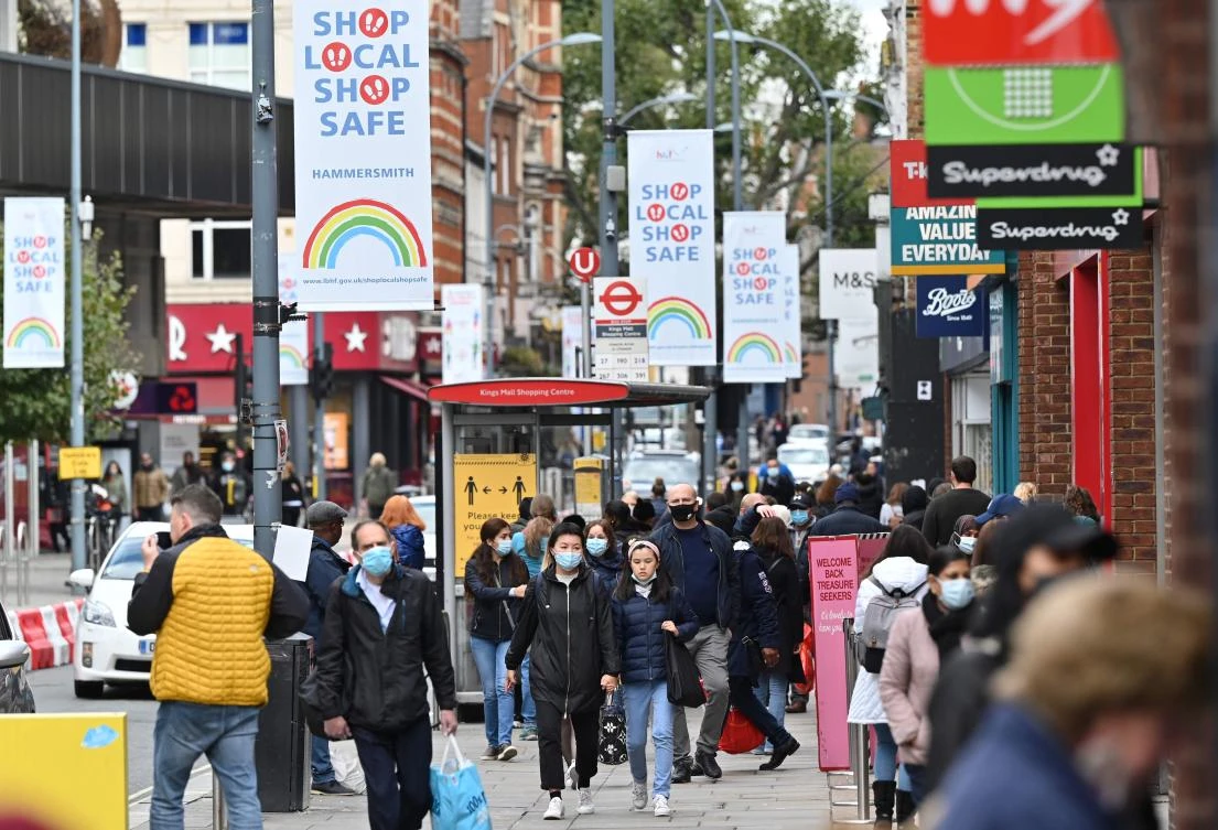 Pedestrians and shoppers walk in the high street in west London on October 11, 2020. (AFP)