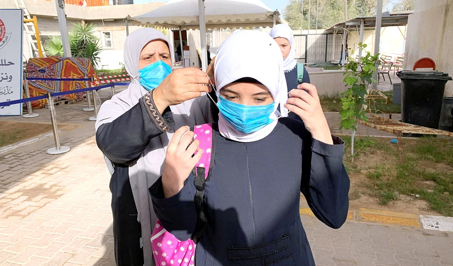 A teacher helps a student to wear a protective mask before entering a school in the Libyan city of Misrata amid concern over the coronavirus crisis. (File/Reuters)