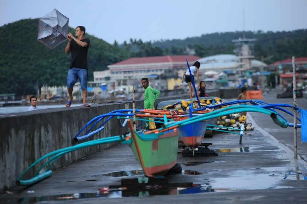 A resident holds onto his umbrella in strong wind as others stand by their wooden boats along the coastal area of Legaspi city in Albay province, southeast of Manila, on October 25, 2020, ahead of tropical storm Molave's expected landfall. (AFP / Charism Sayat)