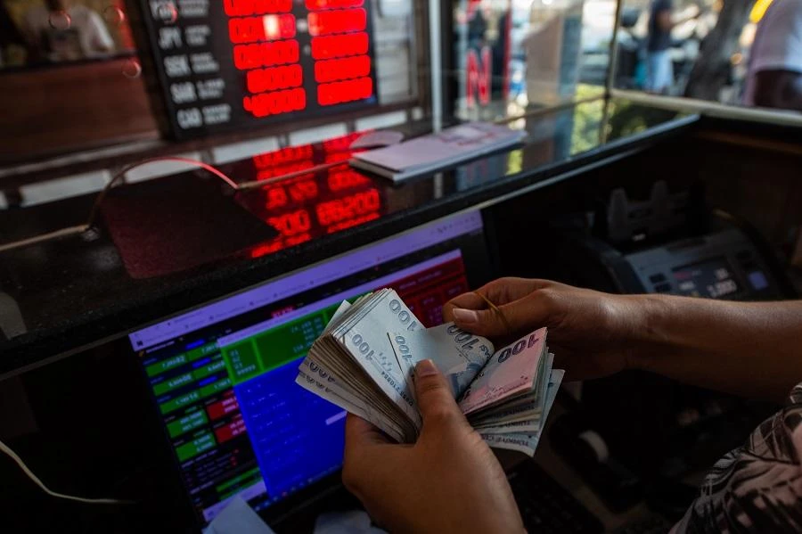A currency exchange office worker counts Turkish Lira banknotes in front of the electronic panel displaying currency exchange rates at an exchange office in Istanbul, on August 6, 2020. (File/AFP)