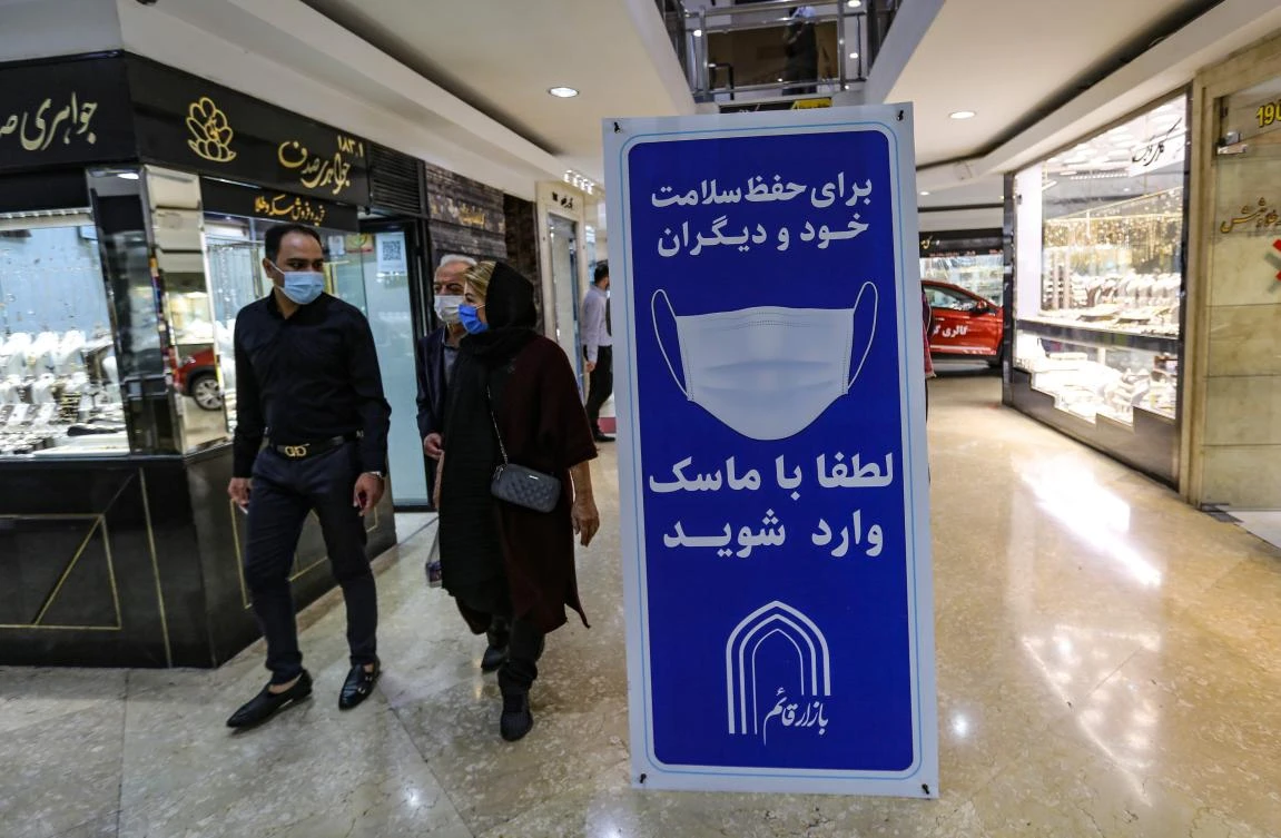 Iranians walk next to a sign advising people to wear masks on their way to shop in Tajrish square in the capital Tehran on Nov. 1, 2020. (AFP)