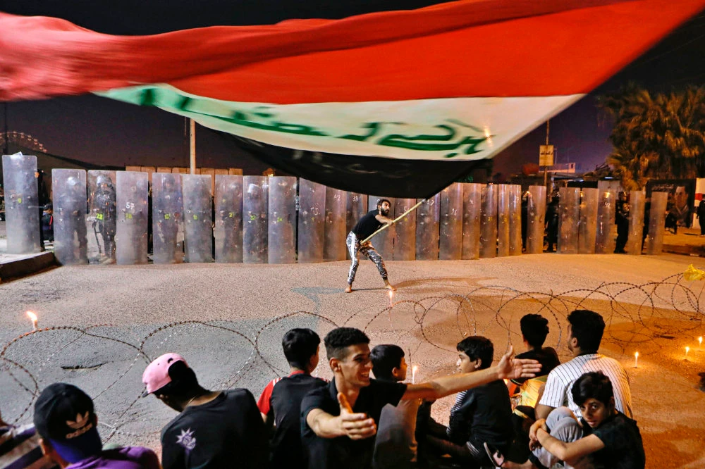 A protester waves an Iraqi flag as security forces surround the protest site during ongoing anti-government demonstrations in Basra, Iraq, on Nov. 4, 2020. (AP Photo/Nabil al-Jurani)