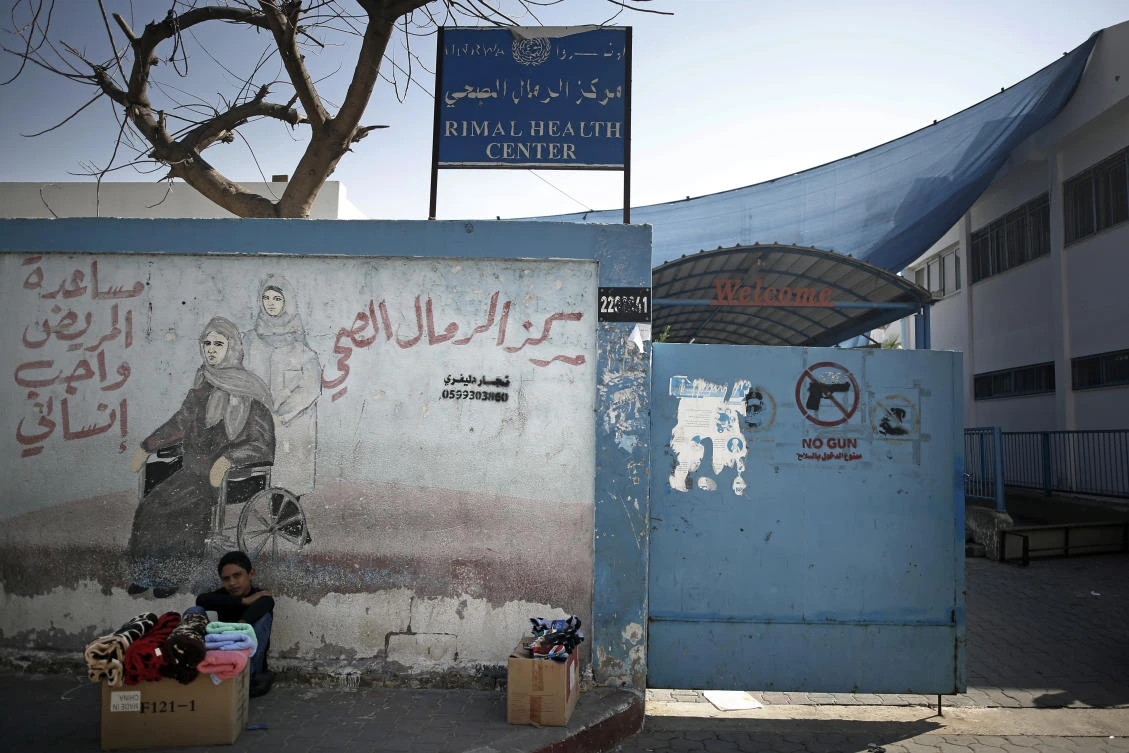 A Palestinian boy displays clothes for sale next to the entrance of the UNRWA Rimal Health Center in Gaza City, Monday, Nov. 9, 2020. (AP)