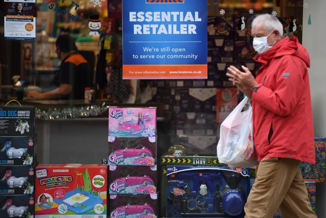 A man walks past a store declaring itself an "essential retailer" in Ashton-under-Lyne east of Manchester in north-west England on November 11, 2020. (AFP)