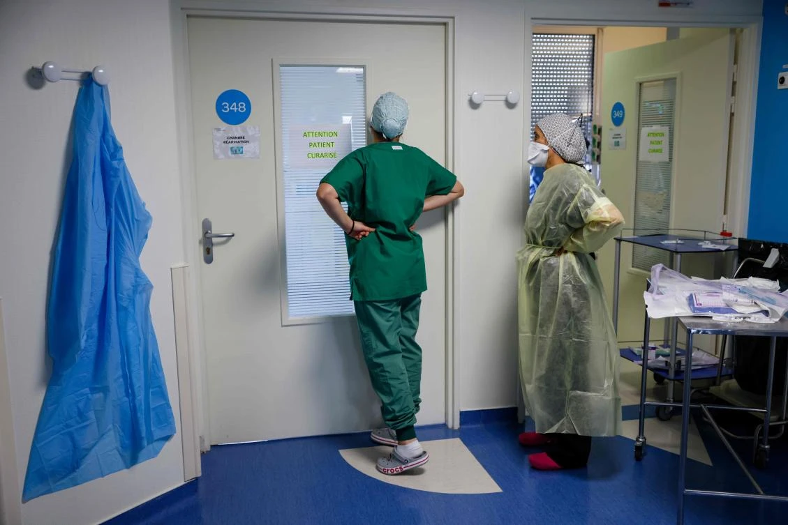 Nurses look through a door at a patient infected with COVID-19 as they lie in an intensive care room of The Estree Private Hospital at Stains, France on November 12, 2020. (AFP)