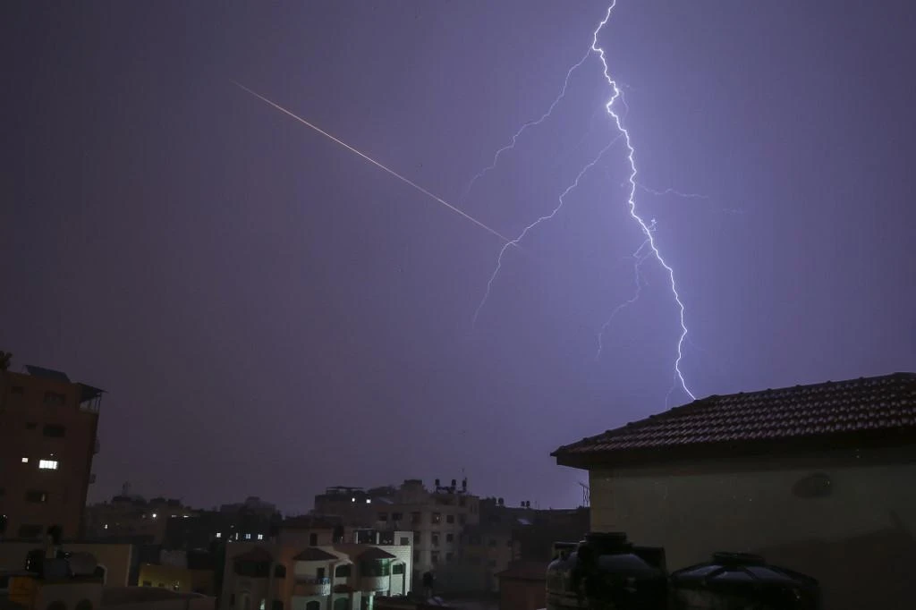 This picture taken from Gaza City shows lightning flashing over buildings as the flair of a rocket launched is seen nearby during a thunderstorm in Gaza city on November 15, 2020. (AFP)