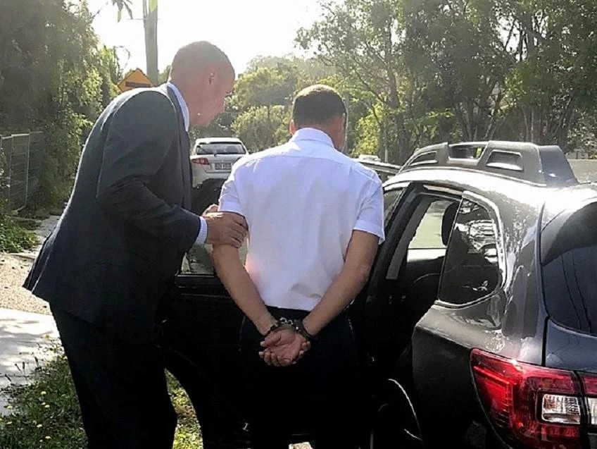 A handout photo released by the Australian Federal Police shows a handcuffed man being taken away after his arrest in Brisbane taken on Nov. 18, 2020. (Australian Federal Police via AFP)