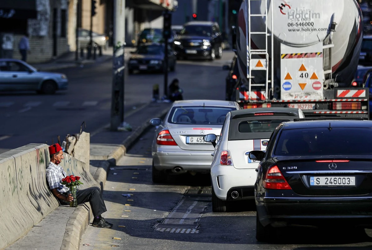 An ambulant flower vendor rests along the side of a road by vehicles waiting at a traffic light in Lebanon's capital Beirut on November 18, 2020. (AFP)