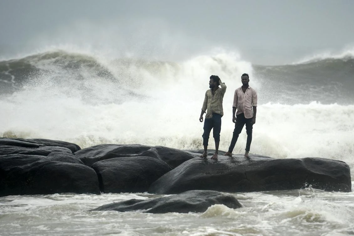 People stand on a rock while waves lashes over at Kovalam beach as cyclone Nivar approaches the eastern Indian coast, in Chennai on November 24, 2020. (AFP)