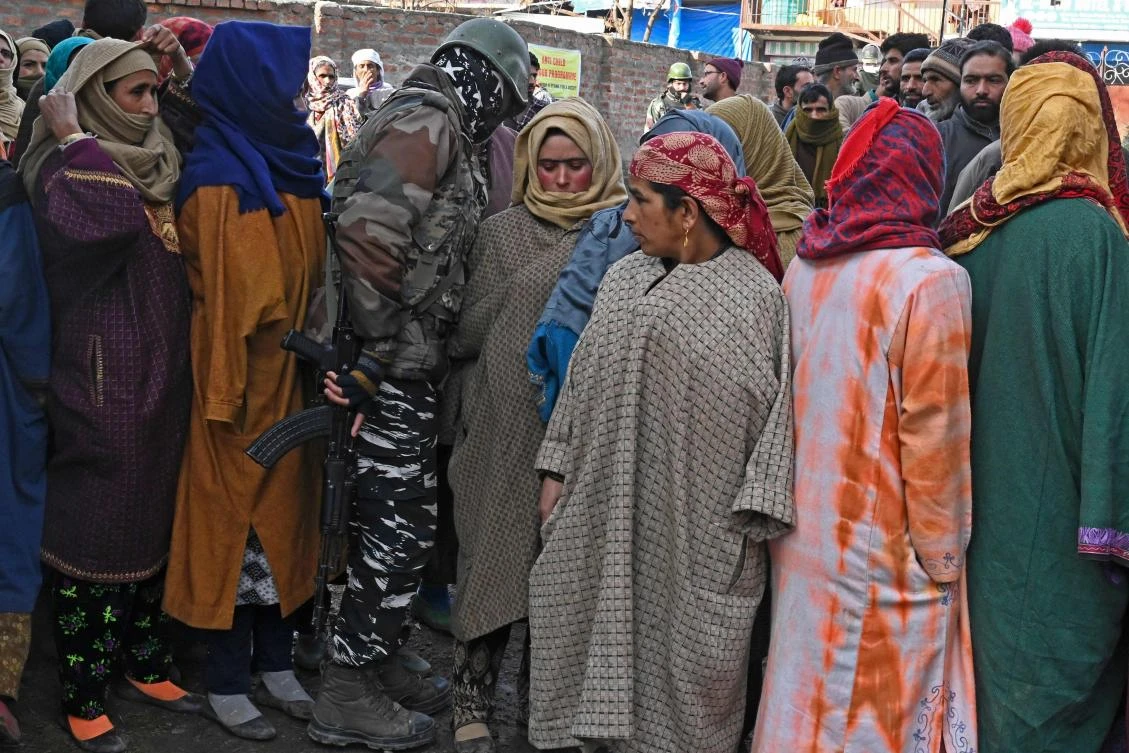 An Indian paramilitary soldier walks next to voters standing in a queue to cast their ballots during the first phase of the District Development Council (DDC) and Panchayat by-elections at a polling station in Raiyar-ICH Khansahib in Budgam district on Nov. 28, 2020. (AFP)