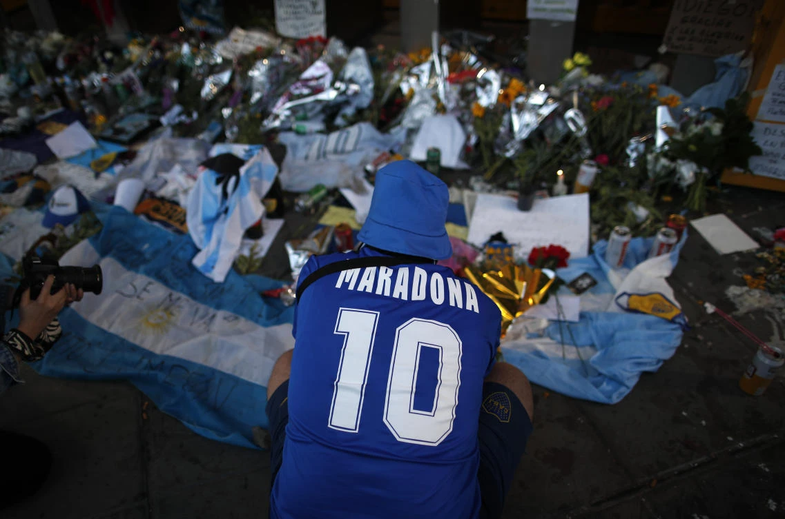A fan mourns in front of flowers and posters left in tribute to Diego Maradona at the entrance of the Boca Juniors stadium known as La Bombonera in Buenos Aires, Argentina, Friday, Nov. 27, 2020. (AP)