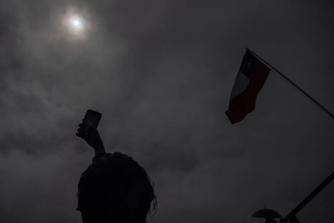 A man takes pictures of the total solar eclipse in Pucon, southern Chile, on December 14, 2020. The hopes of thousands of tourists and residents in Chile's south saw their hopes of watching a total eclipse of the sun shrink as heavy rain fell on Monday just hours before the expected event.MARTIN BERNETTI / AFP