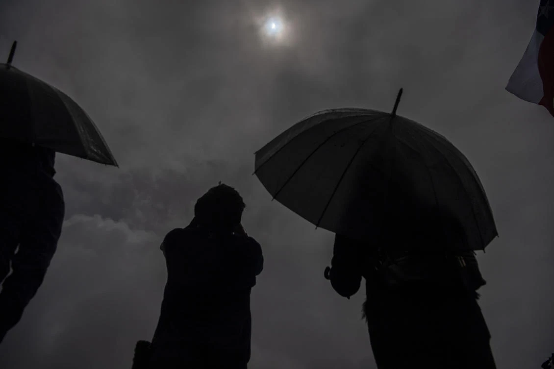 People watch the total solar eclipse on the banks of Villarrica lake in Pucon, southern Chile, on December 14, 2020. The hopes of thousands of tourists and residents in Chile's south saw their hopes of watching a total eclipse of the sun shrink as heavy rain fell on Monday just hours before the expected event.Martin BERNETTI / AFP