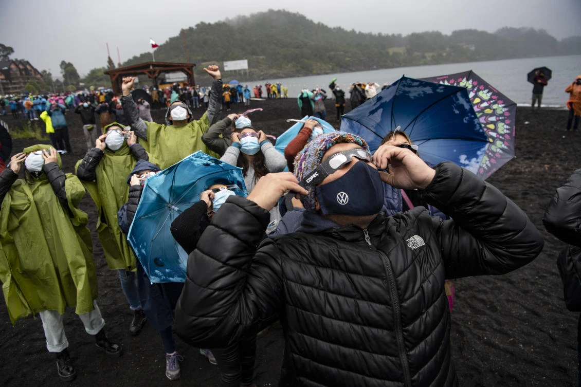 People watch the total solar eclipse on the banks of Villarrica lake in Pucon, southern Chile, on December 14, 2020. The hopes of thousands of tourists and residents in Chile's south saw their hopes of watching a total eclipse of the sun shrink as heavy rain fell on Monday just hours before the expected event.Martin BERNETTI / AFP
