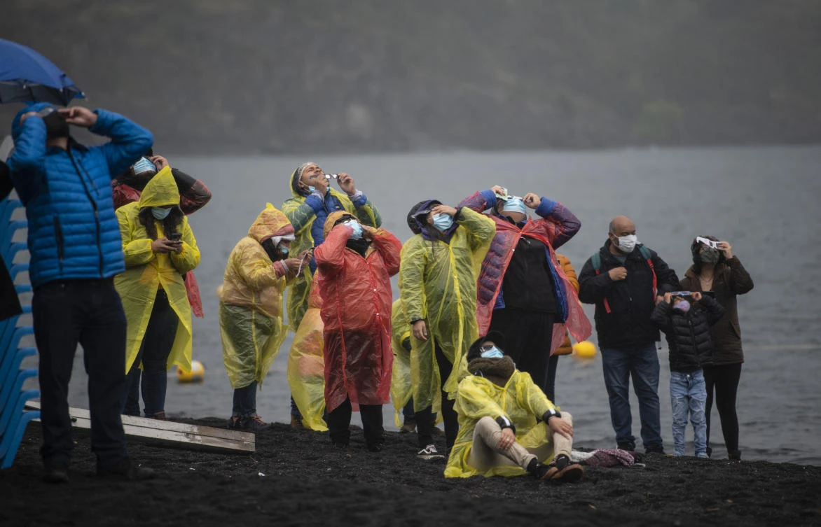 People watch the total solar eclipse on the banks of Villarrica lake in Pucon, southern Chile, on December 14, 2020. The hopes of thousands of tourists and residents in Chile's south saw their hopes of watching a total eclipse of the sun shrink as heavy rain fell on Monday just hours before the expected event.Martin BERNETTI / AFP