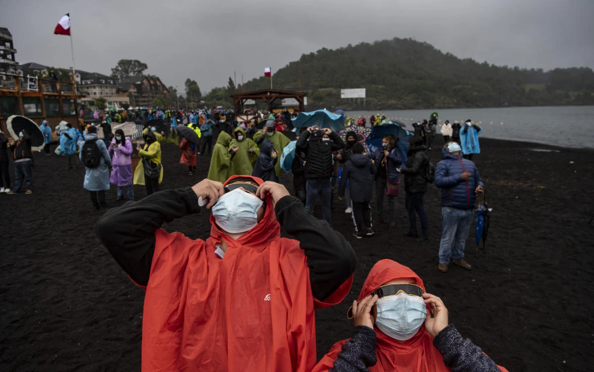 People watch the total solar eclipse on the banks of Villarrica lake in Pucon, southern Chile, on December 14, 2020. The hopes of thousands of tourists and residents in Chile's south saw their hopes of watching a total eclipse of the sun shrink as heavy rain fell on Monday just hours before the expected event.Martin BERNETTI / AFP