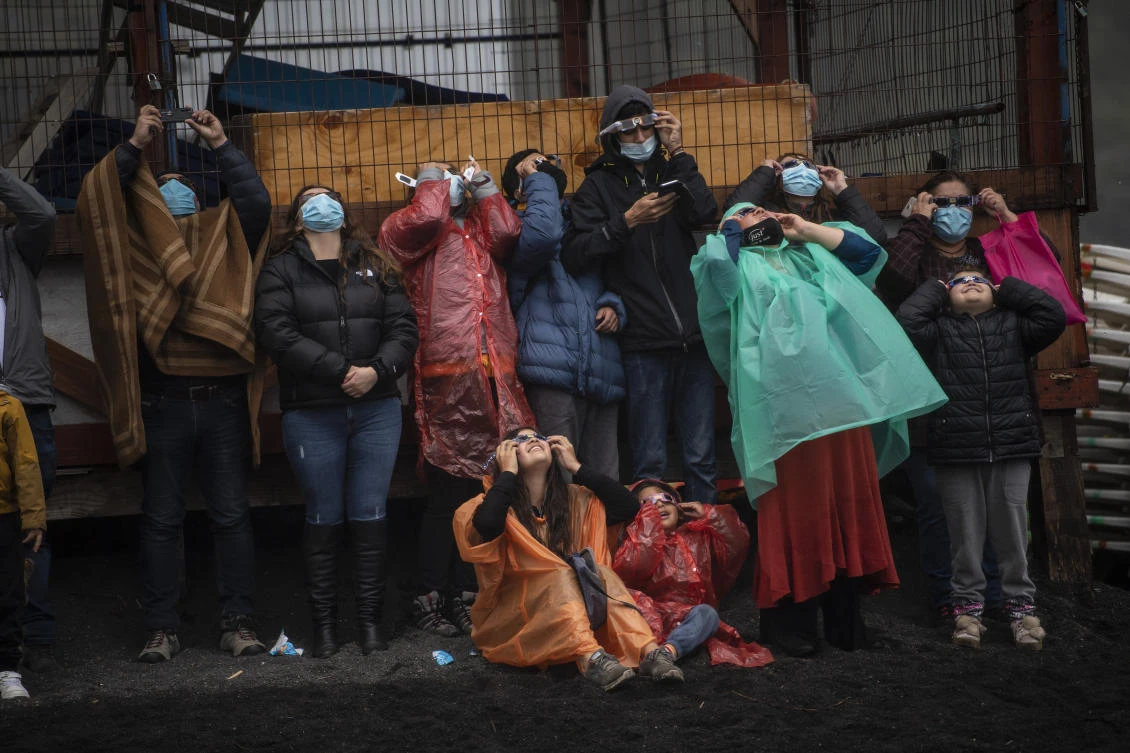 People watch the total solar eclipse on the banks of Villarrica lake in Pucon, southern Chile, on December 14, 2020. The hopes of thousands of tourists and residents in Chile's south saw their hopes of watching a total eclipse of the sun shrink as heavy rain fell on Monday just hours before the expected event.Martin BERNETTI / AFP
