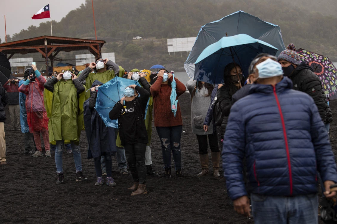 People watch the total solar eclipse on the banks of Villarrica lake in Pucon, southern Chile, on December 14, 2020. The hopes of thousands of tourists and residents in Chile's south saw their hopes of watching a total eclipse of the sun shrink as heavy rain fell on Monday just hours before the expected event.Martin BERNETTI / AFP